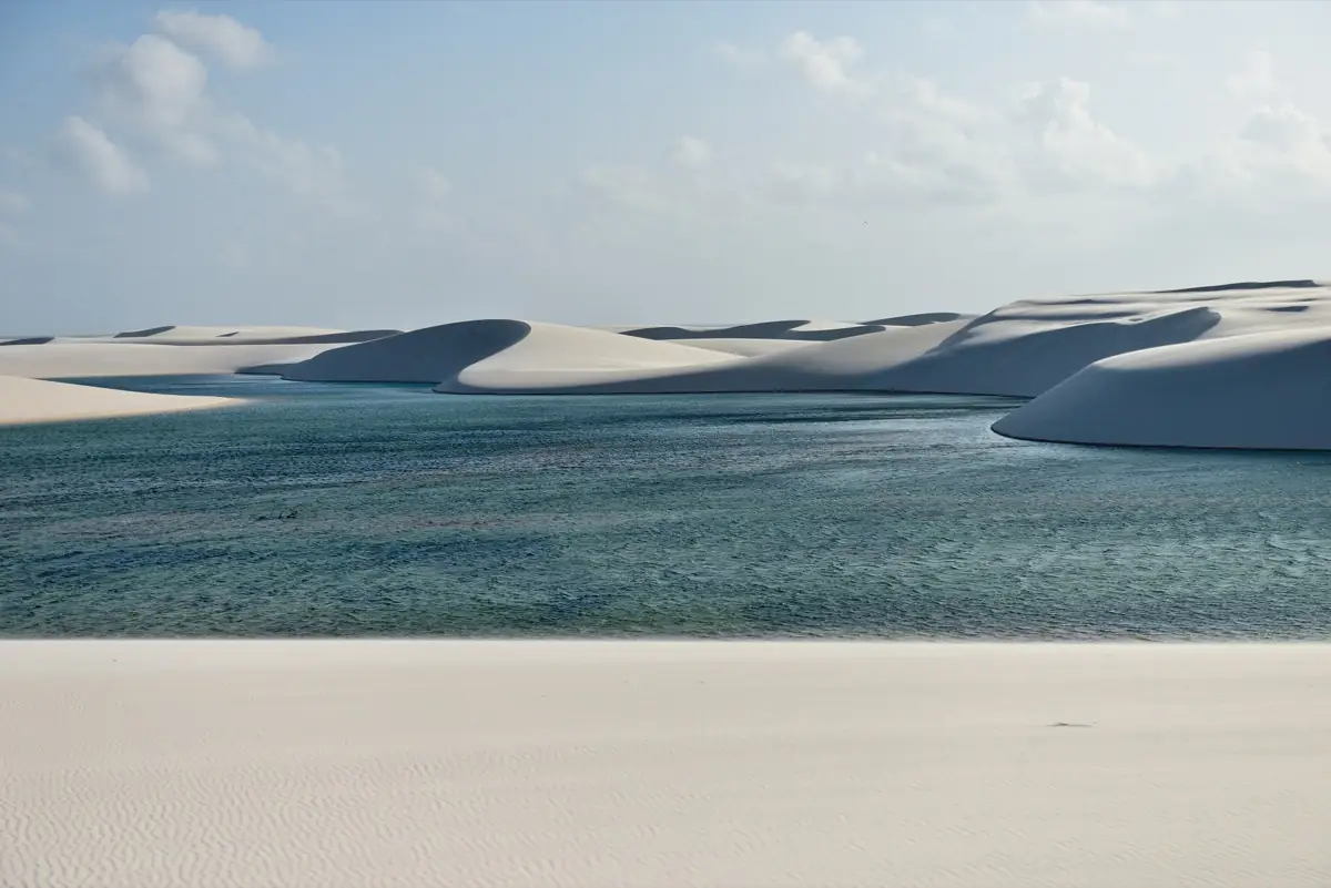Dunas brancas descendo para uma lagoa de água doce no Parque Nacional dos Lençóis Maranhenses